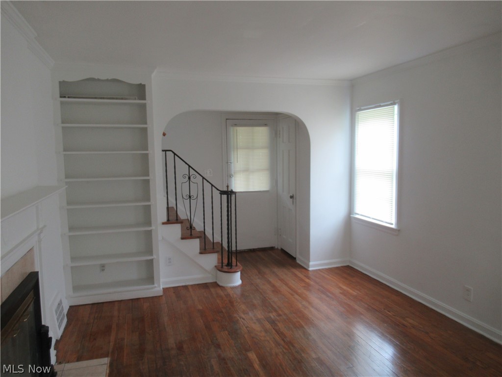 3824 East Antisdale Road Cleveland, OH 44118 - Photo 5 of 27 Living area featuring wood-finish flooring, built-in shelving, a fireplace with a decorative mantel, and an archway leading to a staircase with an ornamental metal railing