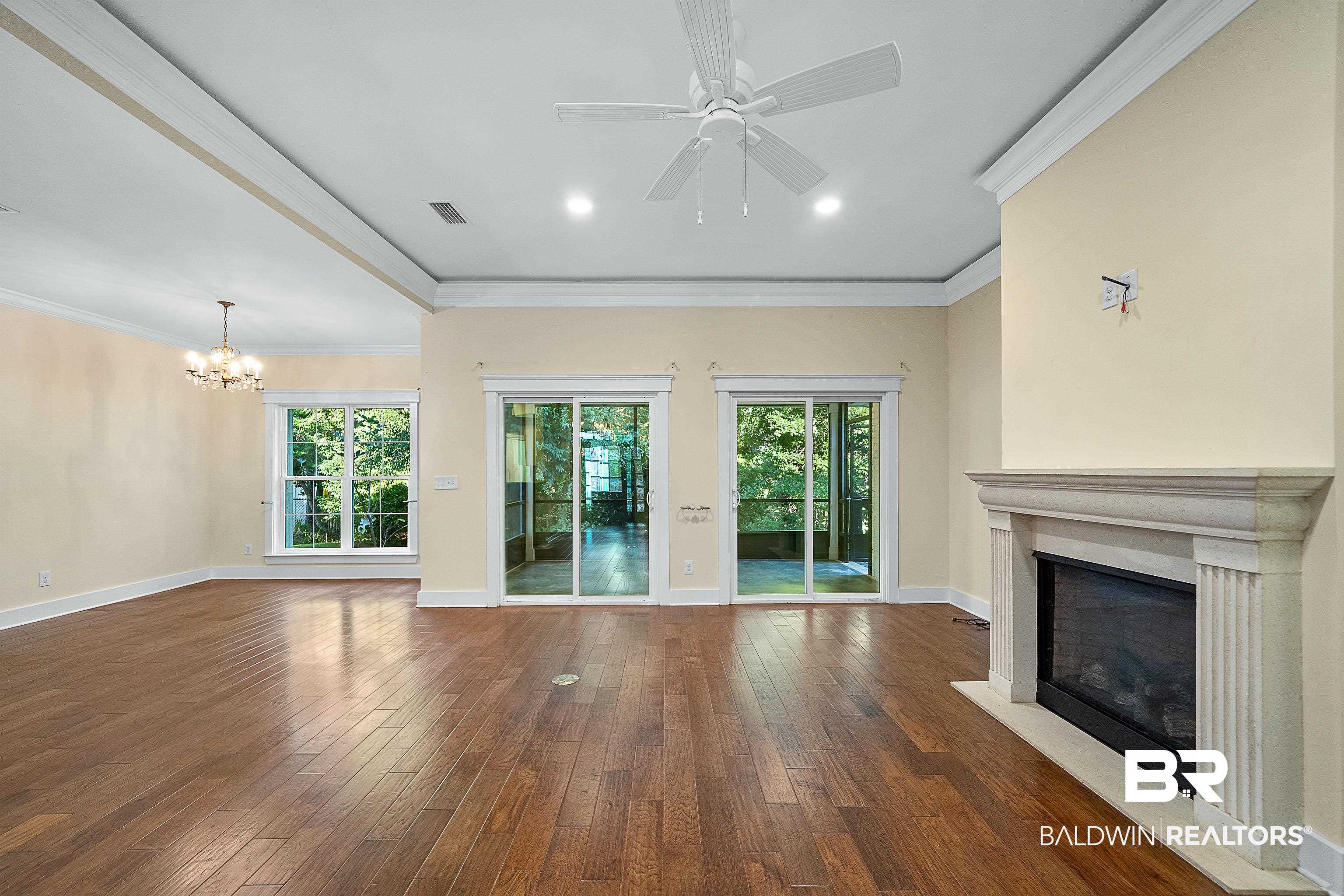 356 Liberty Street Fairhope, AL 36532 - Photo 4 of 39 Unfurnished living room featuring crown molding, a glass covered fireplace, plenty of natural light, dark wood-style floors, and a chandelier