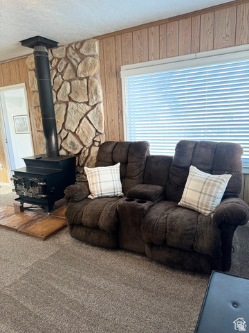 4375 West 4500 S Road Deseret, UT 84624 - Photo 5 of 20 Freestanding wood-burning stove with a stone surround, wood-paneled walls, window with blinds, and neutral carpet flooring
