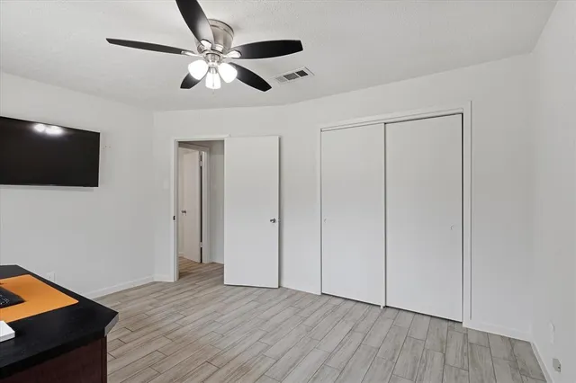 a view of an empty room with wooden floor and a ceiling fan