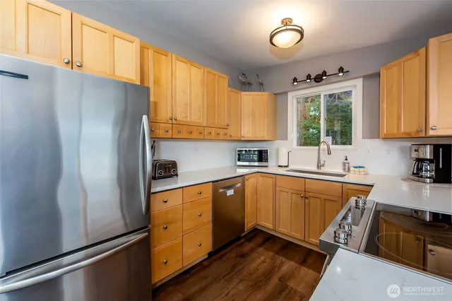 a kitchen with stainless steel appliances granite countertop a refrigerator a sink dishwasher a stove and white countertops with wooden floor