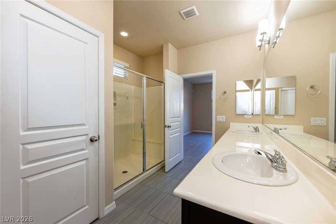 11016 Prairie Grove Road Las Vegas, NV 89179 - Photo 17 of 37 Dual vanities and a glass-enclosed shower create a practical and well-appointed bath space.