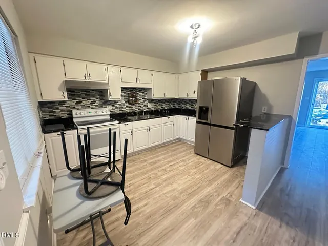 a kitchen with granite countertop a refrigerator stove a sink and white cabinets