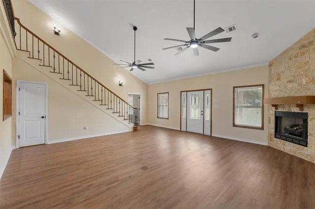 a view of an empty room with wooden floor a ceiling fan and windows