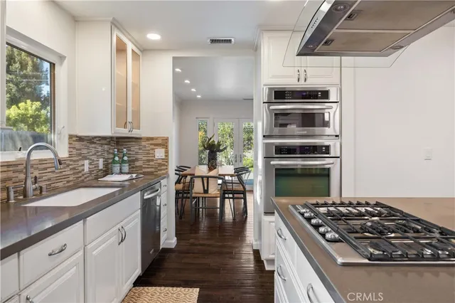 a kitchen with stainless steel appliances a stove a sink dishwasher a refrigerator and a dining table with wooden floor