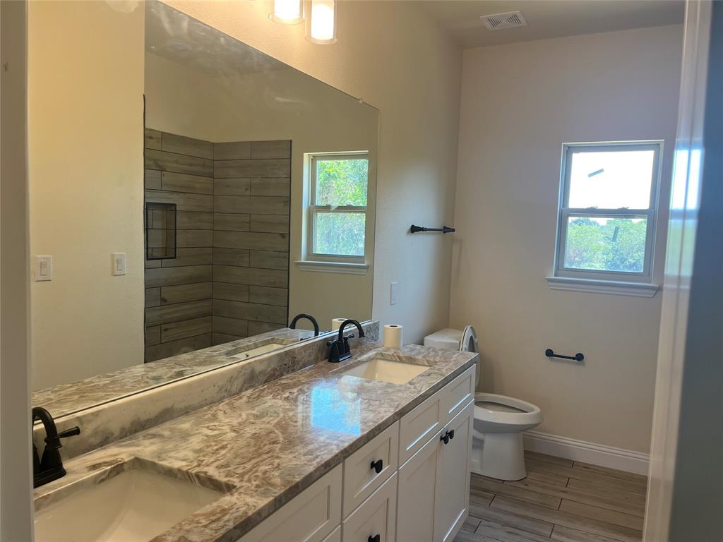 5332 Booker T Street Fort Worth, TX 76105 - Photo 12 of 18 a bathroom with a granite countertop sink a toilet and a window