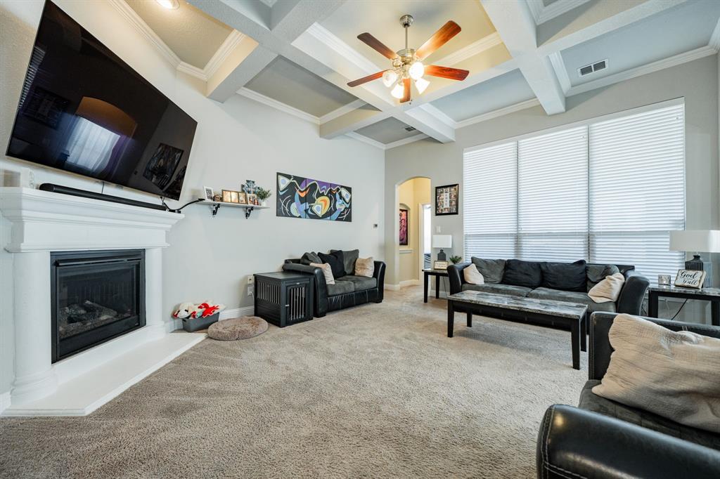 593 Spruce Trail Forney, TX 75126 - Photo 5 of 40 Carpeted living room featuring a fireplace with raised hearth, coffered ceiling, arched walkways, beam ceiling, and crown molding