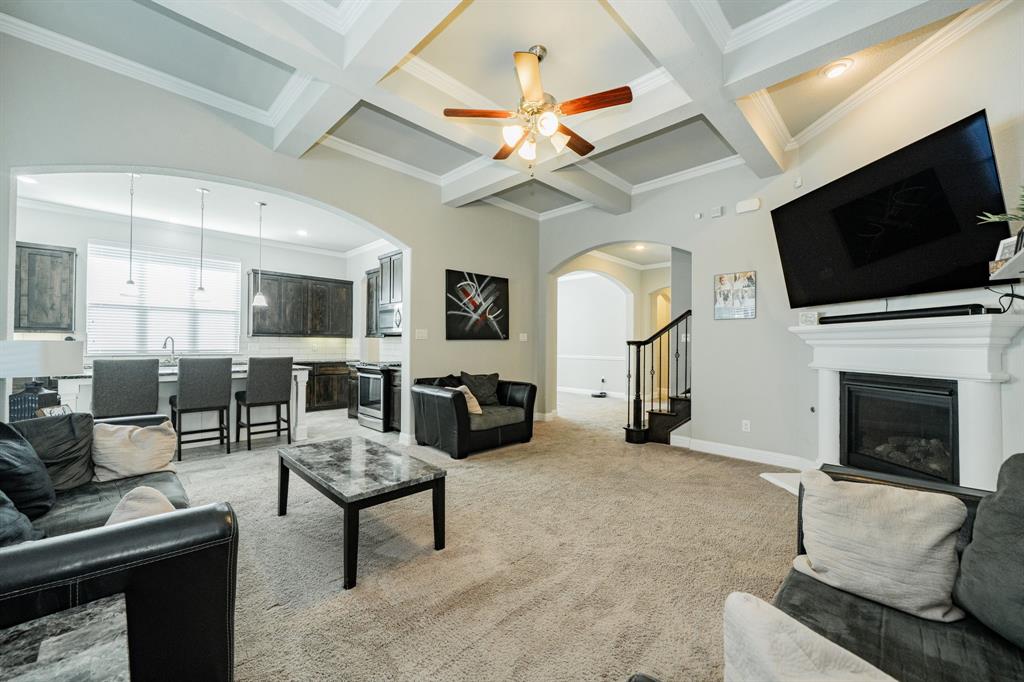 593 Spruce Trail Forney, TX 75126 - Photo 6 of 40 Living room with coffered ceiling, beam ceiling, a glass covered fireplace, light colored carpet, and ornamental molding