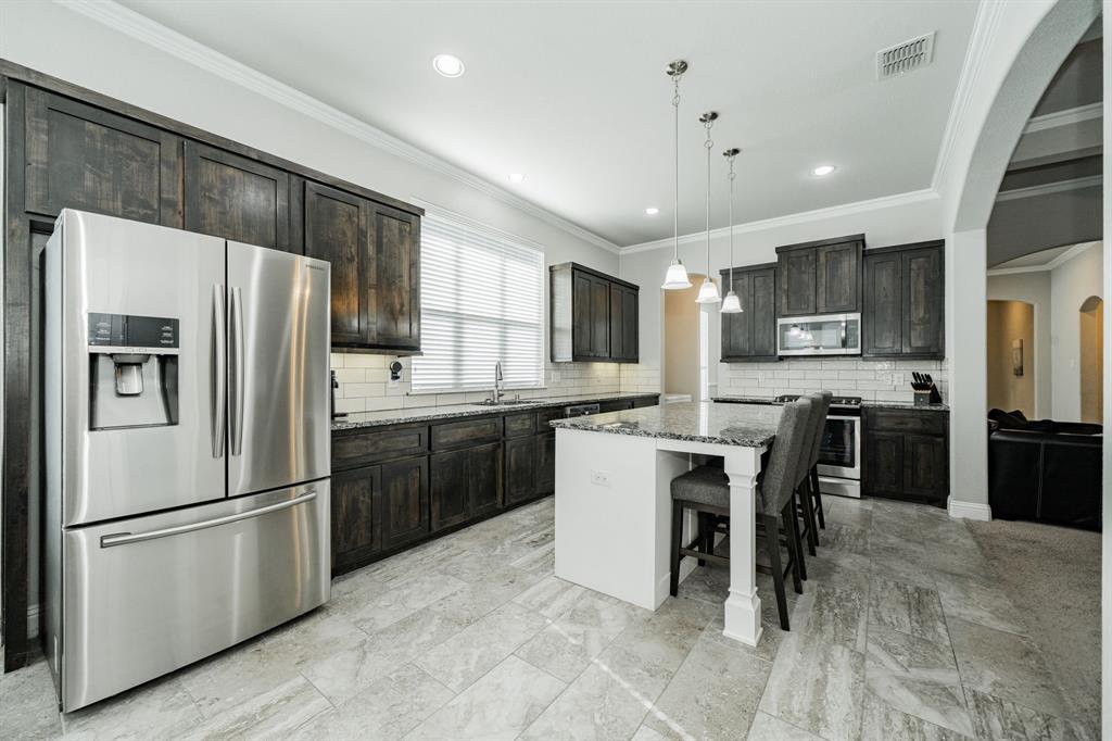 593 Spruce Trail Forney, TX 75126 - Photo 8 of 40 Kitchen featuring stainless steel appliances, arched walkways, a kitchen breakfast bar, dark stone counters, and tasteful backsplash