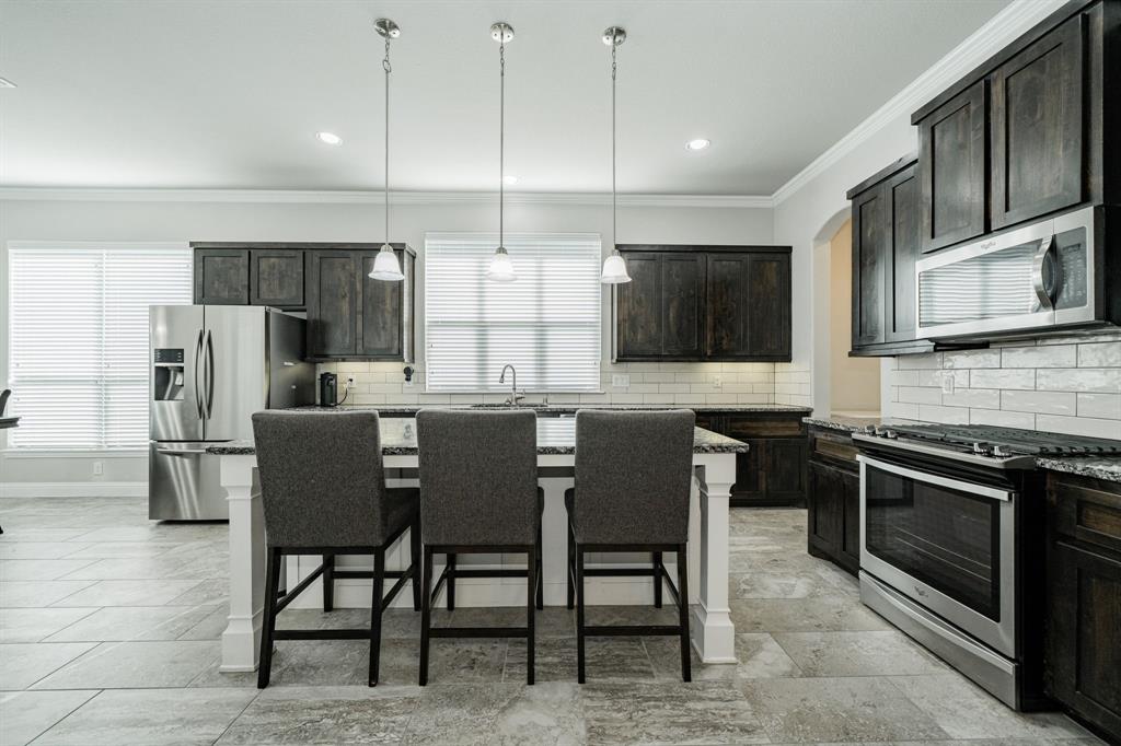 593 Spruce Trail Forney, TX 75126 - Photo 9 of 40 Kitchen with appliances with stainless steel finishes, crown molding, tasteful backsplash, a breakfast bar area, and dark stone counters