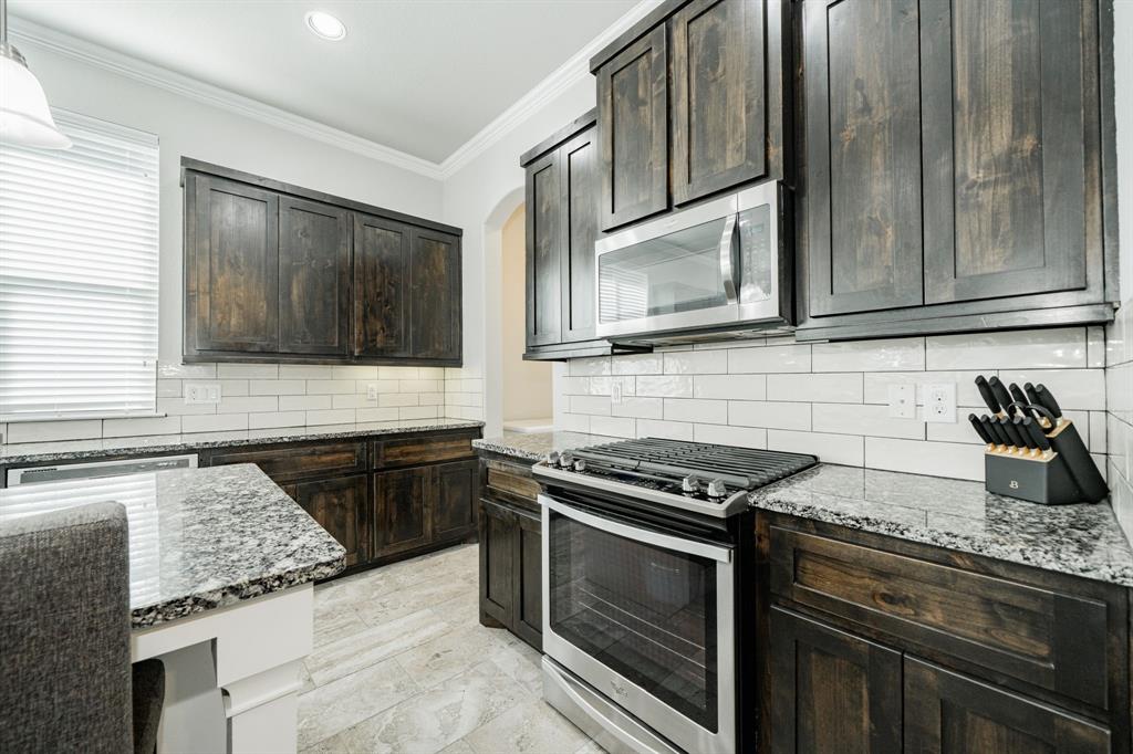 593 Spruce Trail Forney, TX 75126 - Photo 10 of 40 Kitchen with appliances with stainless steel finishes, light stone counters, ornamental molding, dark brown cabinetry, and decorative backsplash