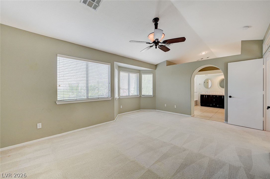 9301 Magic Flower Avenue Las Vegas, NV 89134 - Photo 46 of 70 This spacious primary bedroom features carpet flooring and an arched entryway leading to the primary bathroom.