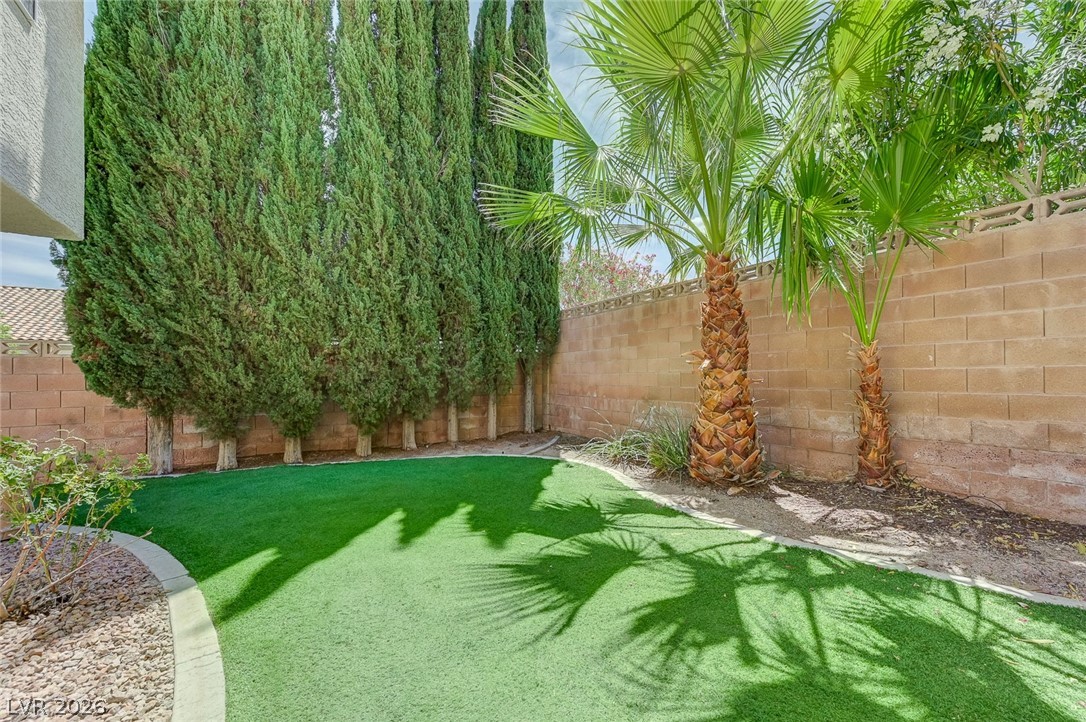 9301 Magic Flower Avenue Las Vegas, NV 89134 - Photo 63 of 70 This private yard boasts lush green turf, tall privacy trees, and tropical palms, creating a serene outdoor space.