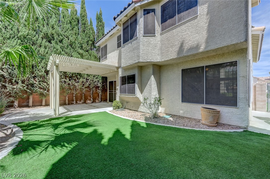 9301 Magic Flower Avenue Las Vegas, NV 89134 - Photo 65 of 70 This house features a charming pergola, lush artificial turf, and stucco siding, creating a delightful outdoor space.