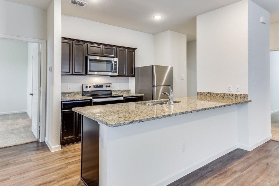 205 Briar Cove Anna, TX 75409 - Photo 8 of 11 Kitchen featuring a peninsula, light stone countertops, appliances with stainless steel finishes, dark brown cabinetry, and light wood finished floors