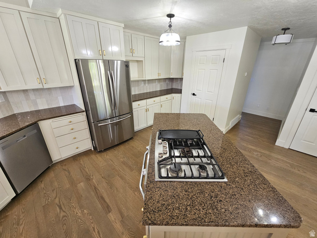 812 East Bates Cyn Road Tooele, UT 84074 - Photo 20 of 144 Kitchen featuring an island with an integrated gas cooktop, white cabinetry with gold-tone hardware, stainless steel appliances, speckled countertops, and wood-finish flooring