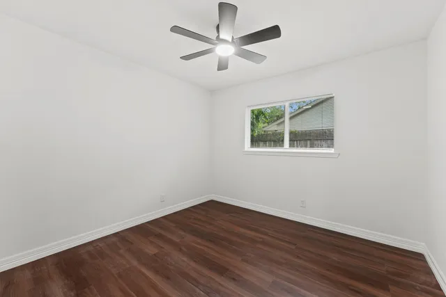 an empty room with wooden floor chandelier fan and windows