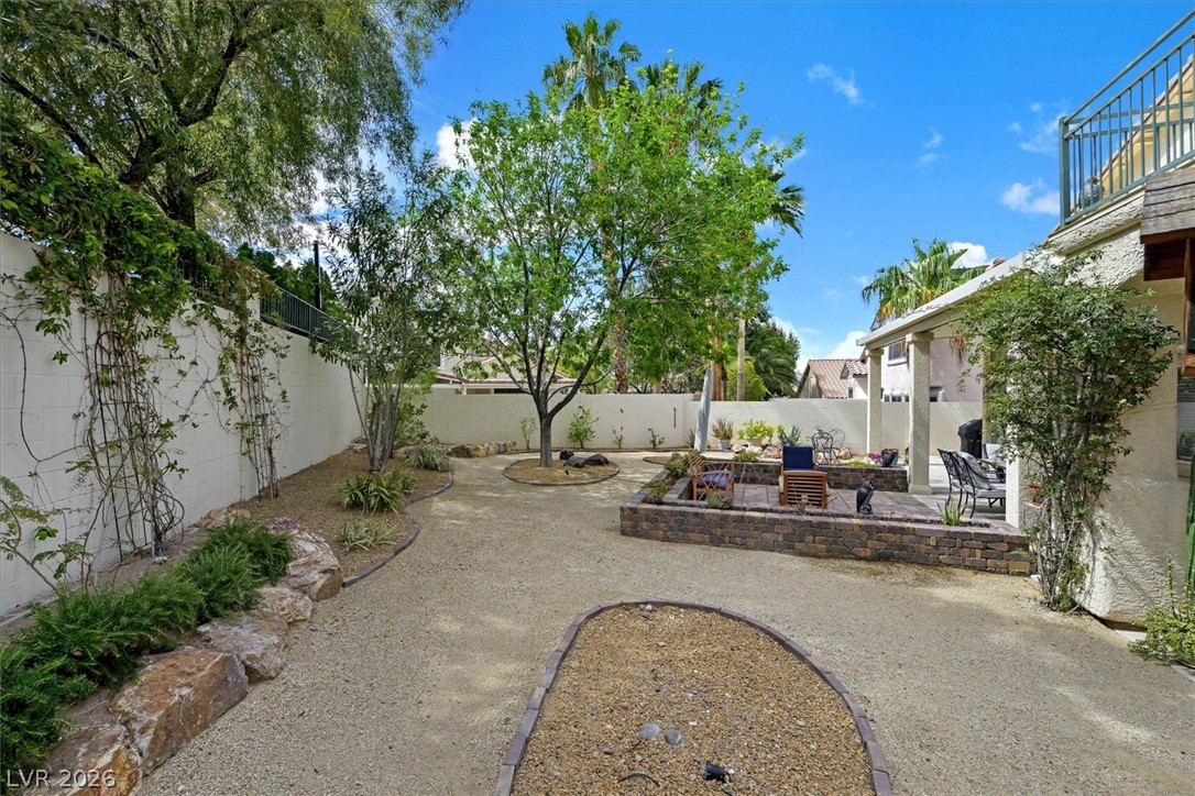 1259 Moon Vision Street Henderson, NV 89052 - Photo 38 of 53 An inviting backyard oasis features a paved patio area, verdant trees, and mature landscaping.