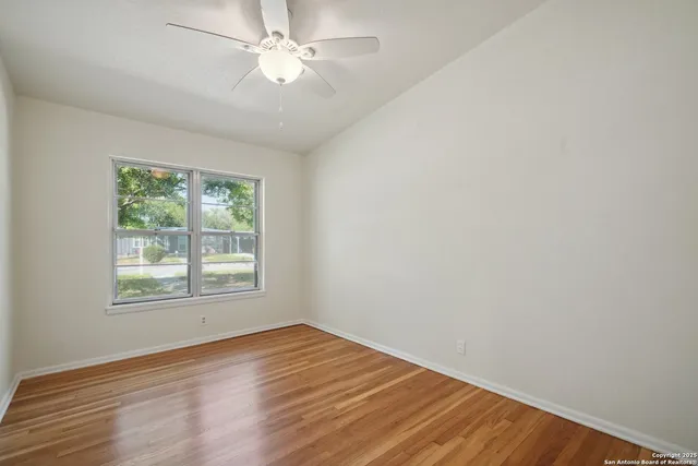 an empty room with wooden floor fan and windows