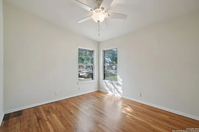 an empty room with wooden floor chandelier fan and windows