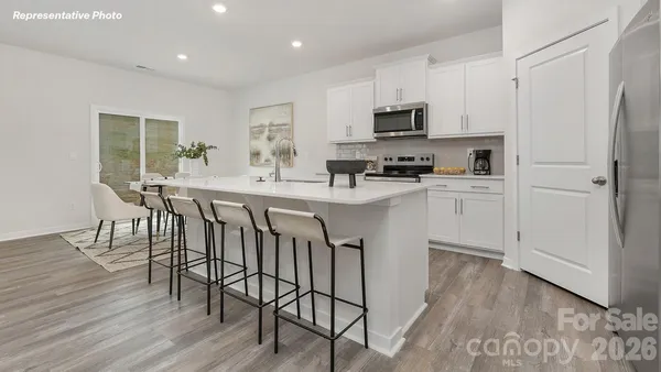 a kitchen with stainless steel appliances granite countertop a stove a sink a microwave a refrigerator with white cabinets and wooden floor