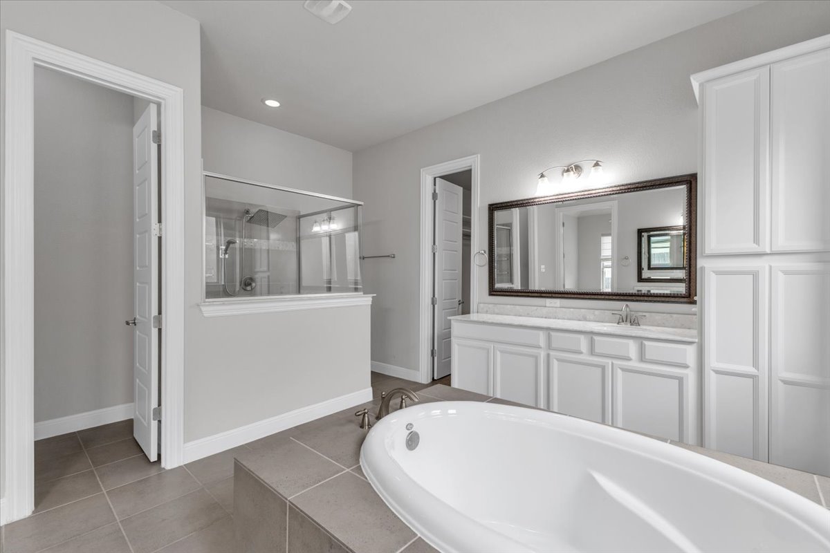 21301 Resource Road Pflugerville, TX 78660 - Photo 15 of 29 Freestanding soaking tub set on a tiled platform, complemented by a glass-enclosed shower with a partial wall