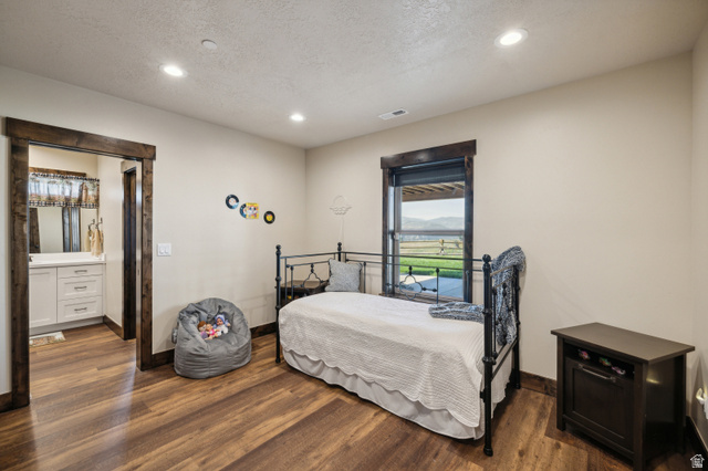 6117 North Rocky Ridge Road Peoa, UT 84061 - Photo 66 of 82 Bedroom featuring wood-finish flooring, recessed lighting, a window with dark trim, and a doorway with dark wood trim leading to a bathroom with a white vanity and mirror