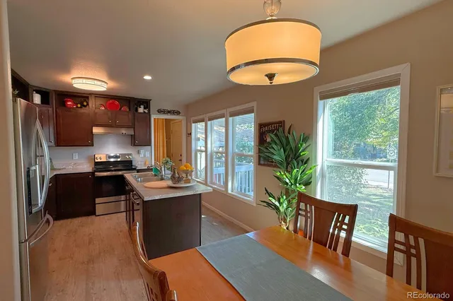 a kitchen with stainless steel appliances granite countertop a stove a refrigerator a sink a dining table and chairs with wooden floor