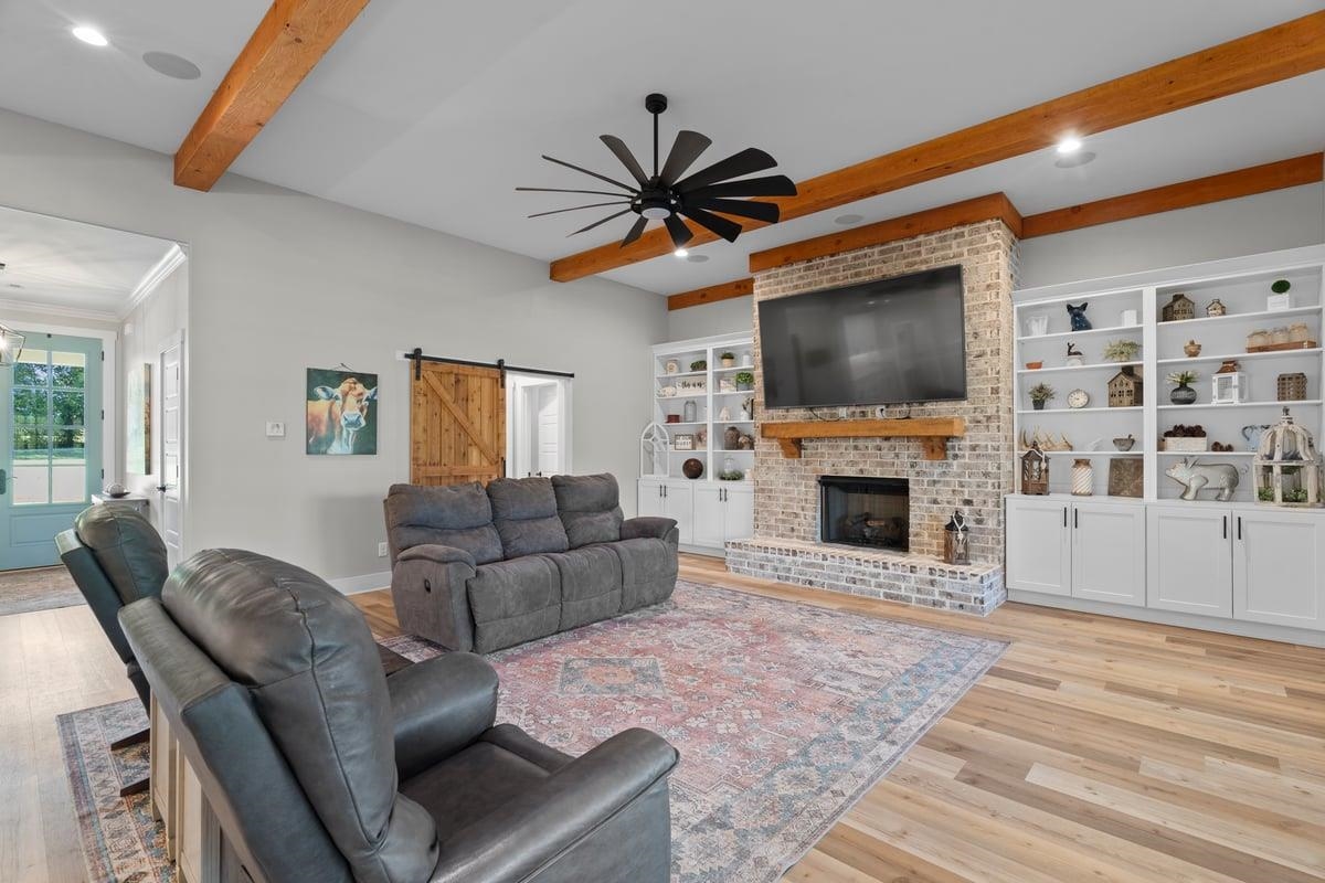 678 Morris Road Covington, TN 38019 - Photo 12 of 40 Den with beam ceiling, built ins, a barn door leading to BR 2 suite, a ceiling fan, light wood finished floors, and a fireplace