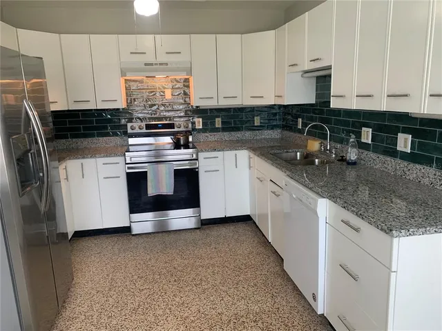 a kitchen with stainless steel appliances granite countertop a stove a sink and white cabinets