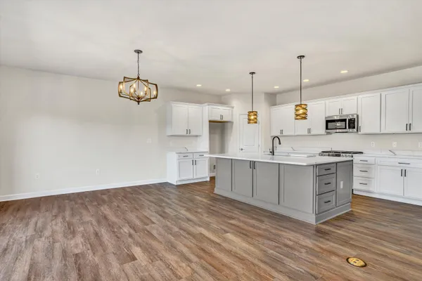 a large white kitchen with kitchen island a sink dishwasher a stove and white cabinets with wooden floor