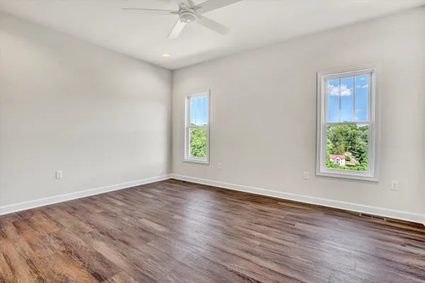 an empty room with wooden floor chandelier fan and windows