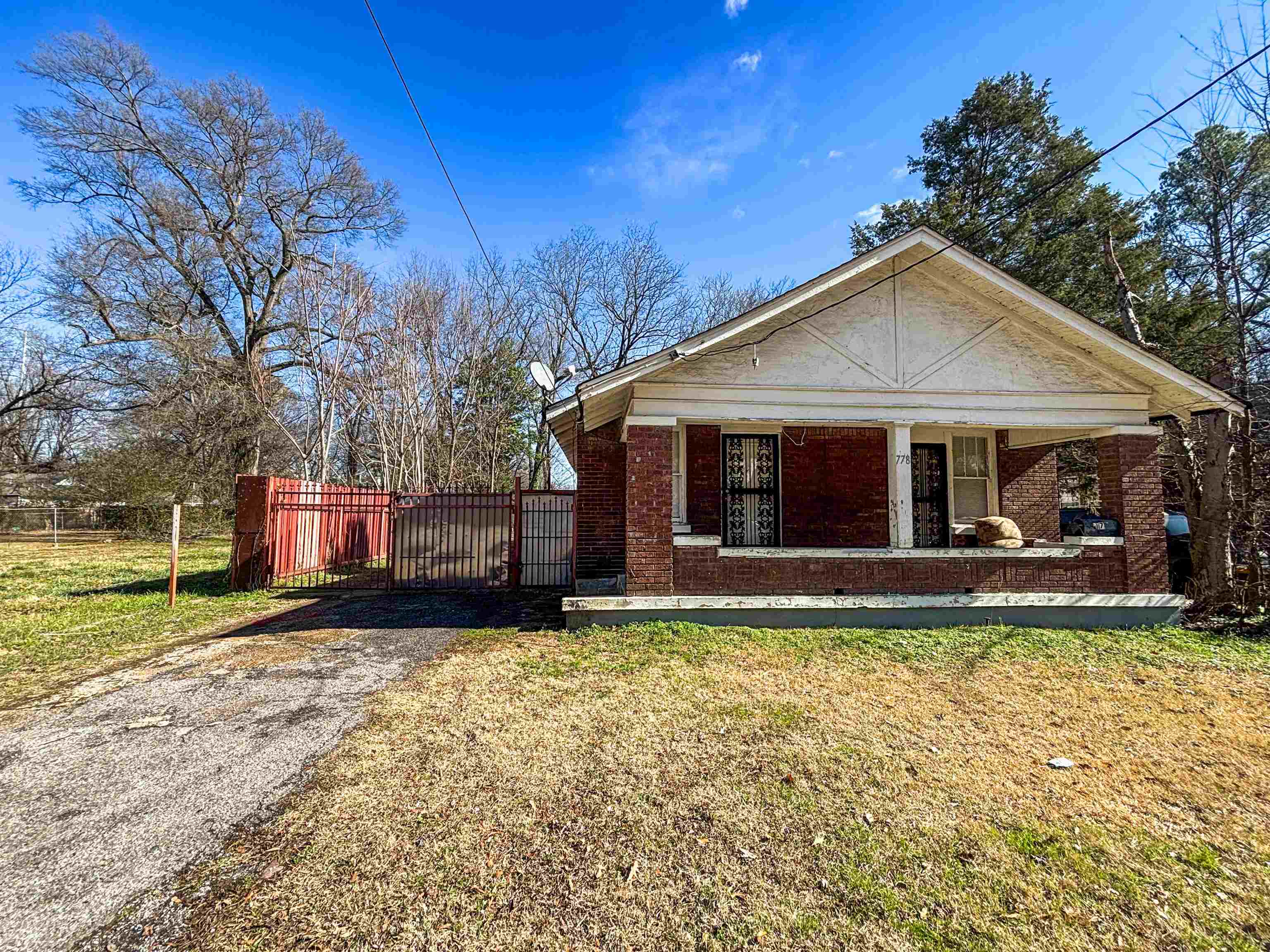 View of front of property featuring covered porch, asphalt driveway, brick siding, and a gate