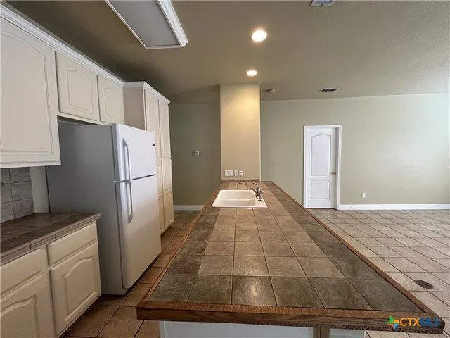 a view of a refrigerator in kitchen and an empty room with wooden floor