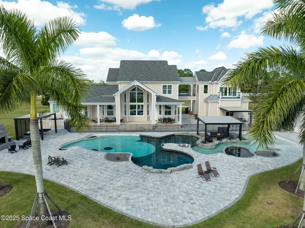 a view of a white house with a swimming pool and lawn chairs under palm trees