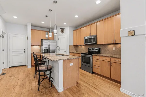 a kitchen with stainless steel appliances granite countertop a stove top oven a sink a dining table and chairs with wooden floor