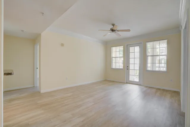 an empty room with wooden floor ceiling fan and windows