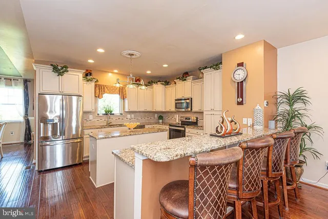 a kitchen with stainless steel appliances granite countertop a refrigerator a sink dishwasher a stove and white countertops with wooden floor