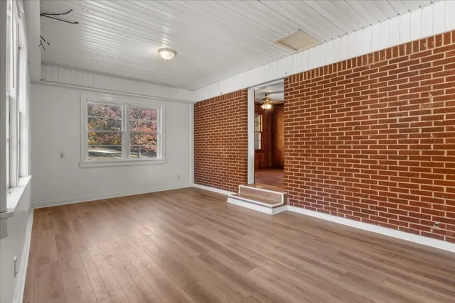 an empty room with wooden floor chandelier fan and windows