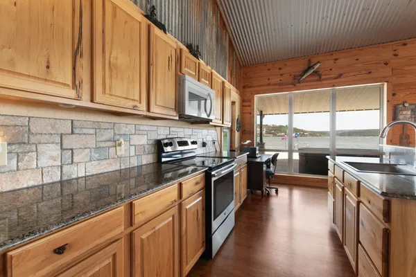 a kitchen with stainless steel appliances granite countertop a sink a oven a dining table and chairs with wooden floor