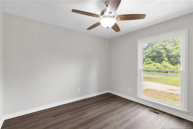 an empty room with wooden floor fan and windows
