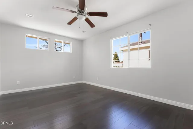 a view of an empty room with wooden floor and a ceiling fan