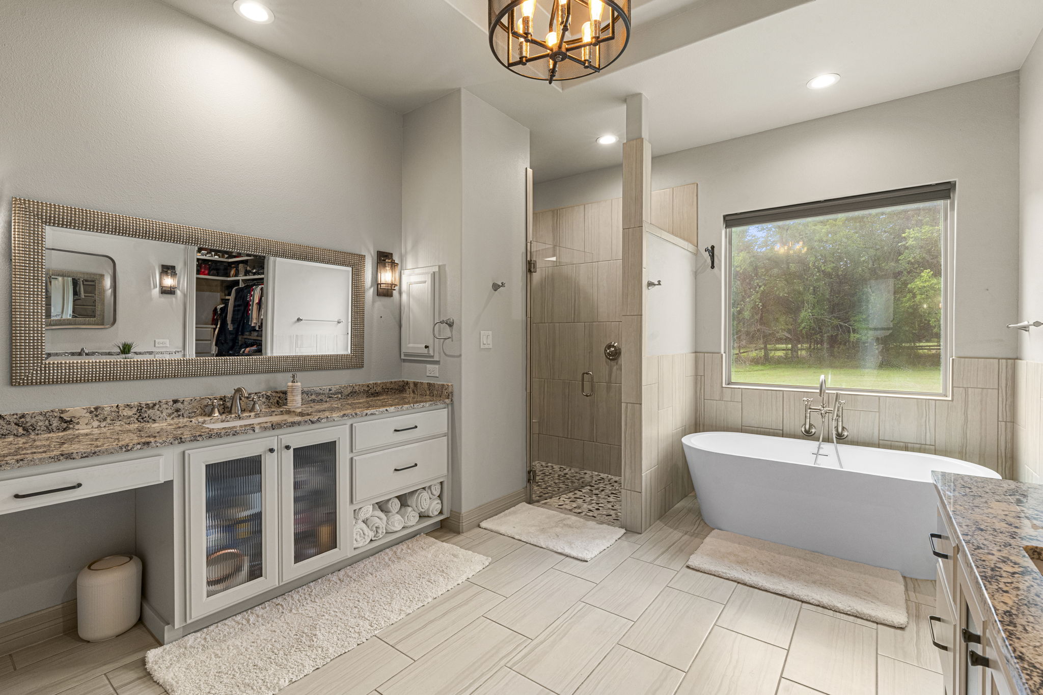 16202 Remuda Trail Buda, TX 78610 - Photo 13 of 40 Primary bathroom features a double vanity with stone countertops and ample storage, a spacious walk-in shower with a glass door, and a freestanding soaking tub situated beneath a large window