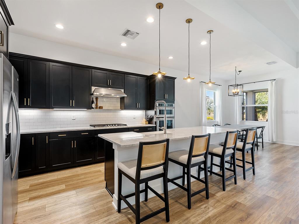 7857 Redonda Loop Lakewood Ranch, FL 34202 - Photo 13 of 51 a kitchen with stainless steel appliances kitchen island granite countertop a table chairs sink and wooden cabinets