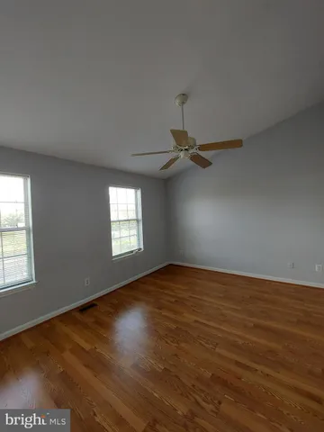 an empty room with wooden floor fan and windows
