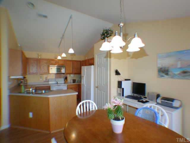 Open kitchen has wood cabinets and plenty of storage; upgrades include built-in microwave and tile backsplash behind stove. Other