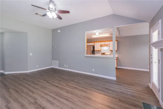 an empty room with wooden floor chandelier fan and windows
