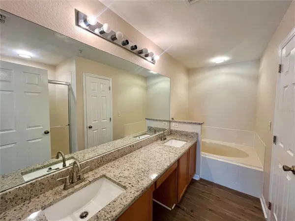 a bathroom with a granite countertop double vanity sink a mirror and a bathtub