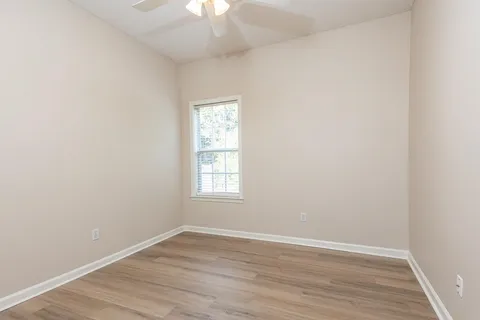 an empty room with wooden floor chandelier fan and window