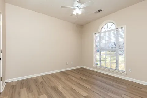 an empty room with wooden floor chandelier fan and windows
